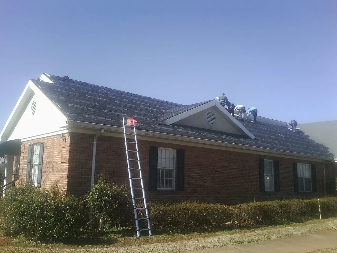 Crew tearing shingles off a brick ranch roof with a ladder set — Metal Roof Repair work by our crew in Careywood