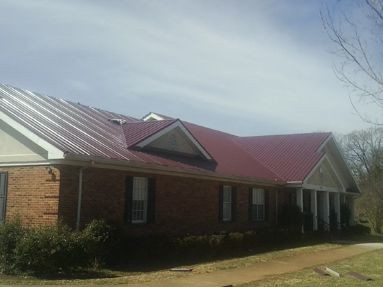 Red metal roof with gabled entries on a long brick building, from a Hail Damage Roof Repair job in Careywood