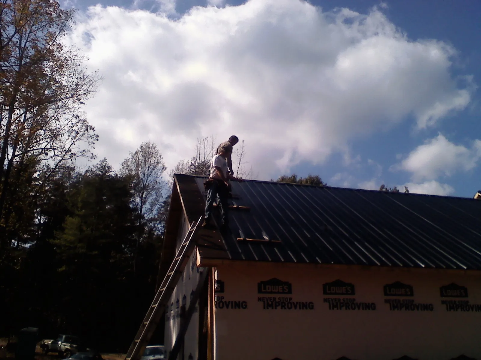 Roofer fastening dark metal panels high against a cloudy sky, from a Roof Inspection job in Careywood