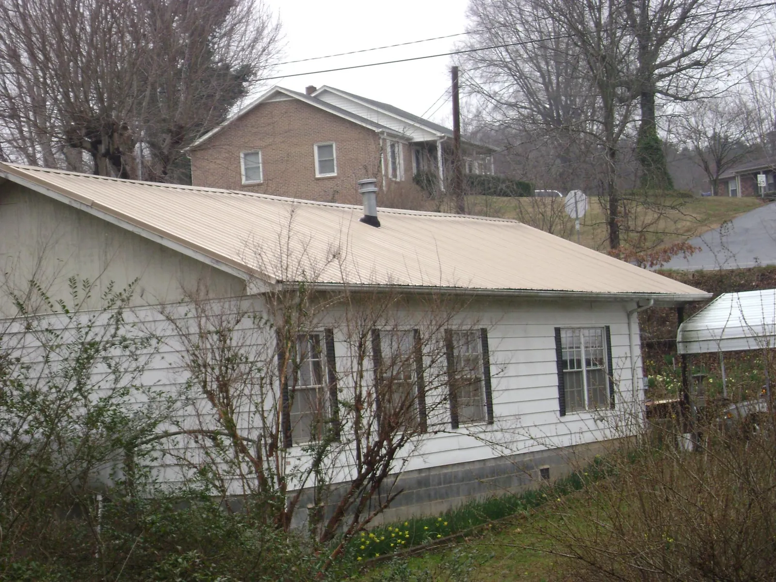 Tan metal roof on a white sided house set into a hillside — Commercial Roofing by Roofing Brothers in Careywood